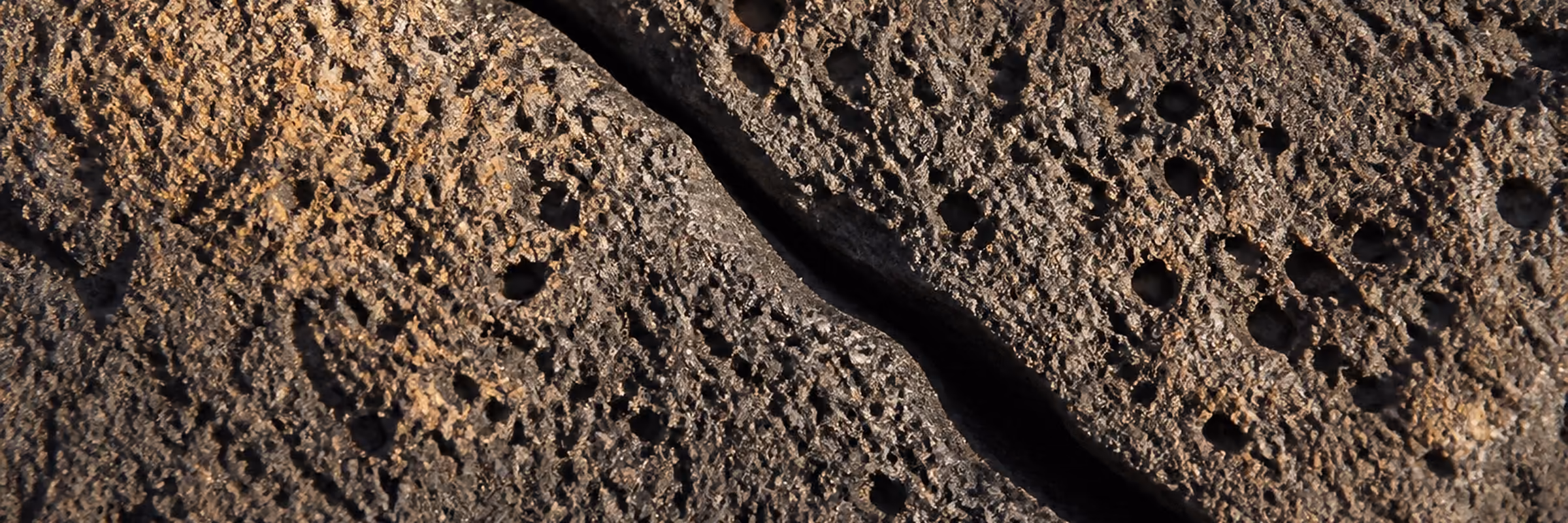 Muro de piedra basáltica con los huecos de gas de la lava, atravesado por la junta seca entre dos bloques