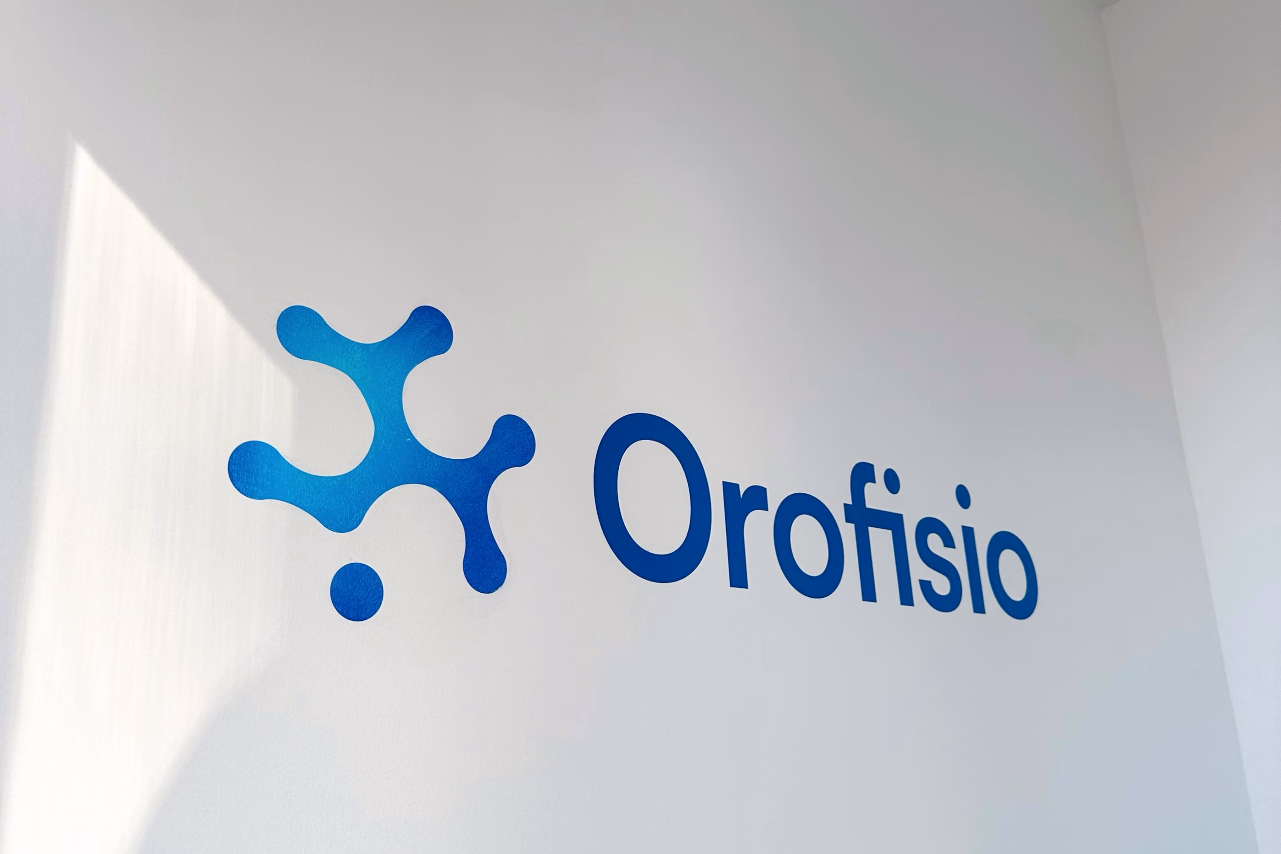 El logotipo de Orofisio sobre una pared blanca atravesada por un haz de luz natural