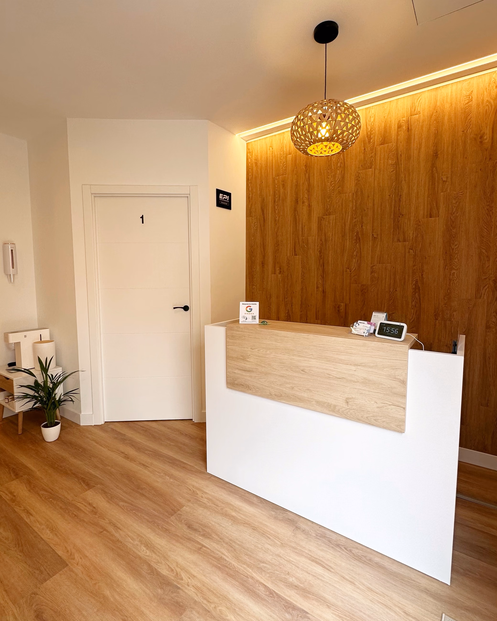 Mostrador de recepción de Orofisio, con el panel de madera y la puerta de la sala al fondo